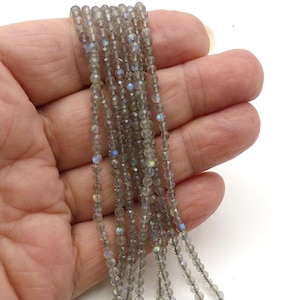 May include: Strands of faceted, gray labradorite beads with flashes of blue and iridescent color. The beads are strung together, creating a delicate and shimmering effect. Ideal for jewelry making.
