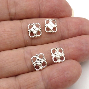 May include: Four small silver-toned metal stud components with intricate openwork designs. Two pieces feature a central square grid pattern, while the other two pieces display a central cluster of five small raised circular dots.