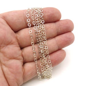 May include: A silver-colored metal chain featuring a series of small, uniform, oval-shaped links connected in a continuous strand. The chain has a polished, reflective finish and is composed of multiple interconnected loops forming a single length.