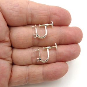May include: Two silver-toned, screw-back earring findings. Each finding has a curved, U-shaped design with a small post and a screw mechanism. The findings are shown against a neutral background.