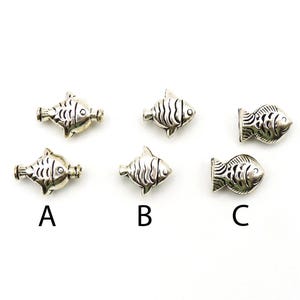 May include: Silver-toned metal fish-shaped beads. The beads have detailed scales and fins. The image includes three different styles of fish beads, labeled A, B, and C. These beads are suitable for jewelry making.