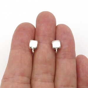 May include: A pair of small, square-shaped silver earring studs with a smooth, polished finish. Each stud features a tiny, integrated loop at the bottom, designed for attaching additional jewelry components or charms to the base of the earring.