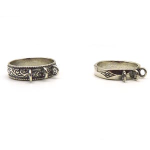 May include: Two silver rings with a collar design are displayed against a white background. One ring features an ornate, swirling pattern, while the other has a simpler design with a diamond-shaped accent. Both rings have small loops.