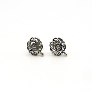 May include: A pair of silver-toned metal earring components featuring an intricate openwork leaf or floral pattern with swirling filigree details and a small circular loop at the base for attaching additional jewelry elements or charms.
