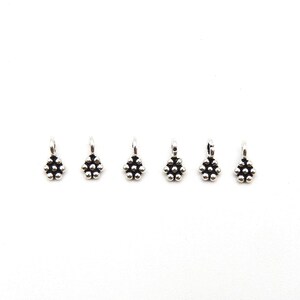 May include: Six small silver-toned metal charms, each shaped like a tiny flower with a central bead surrounded by six smaller beads. Each charm features a small loop at the top for attachment, with a polished finish and dark recessed detailing.