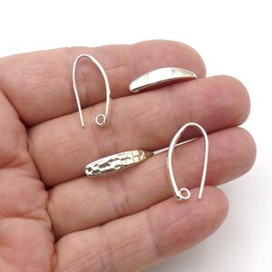 May include: Close-up of silver earring components. The image shows two silver earring hooks, a small silver curved bar, and a silver earring component with a textured, hammered gold-colored end.