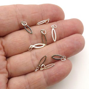 May include: A collection of small, silver-colored metal charms, each featuring a simple, elongated, open marquise or eye-shaped frame with a small circular jump ring attached at the top for easy connection to jewelry or other craft projects.
