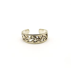 May include: A silver-colored toe ring with an open design. The ring features a continuous, swirling pattern. The band is adjustable, with open ends. The jewelry is set against a white background.
