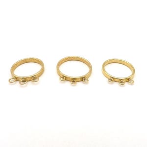 May include: Three gold-colored rings with textured surfaces and small loops attached. The rings are arranged on a white background, showcasing their design and potential for jewelry making or crafting.