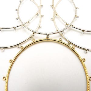 May include: A collection of circular metal hoops featuring a textured surface and multiple small loops attached to the outer edge. The set includes one gold-toned hoop and several silver-toned hoops, all arranged in an overlapping pattern.