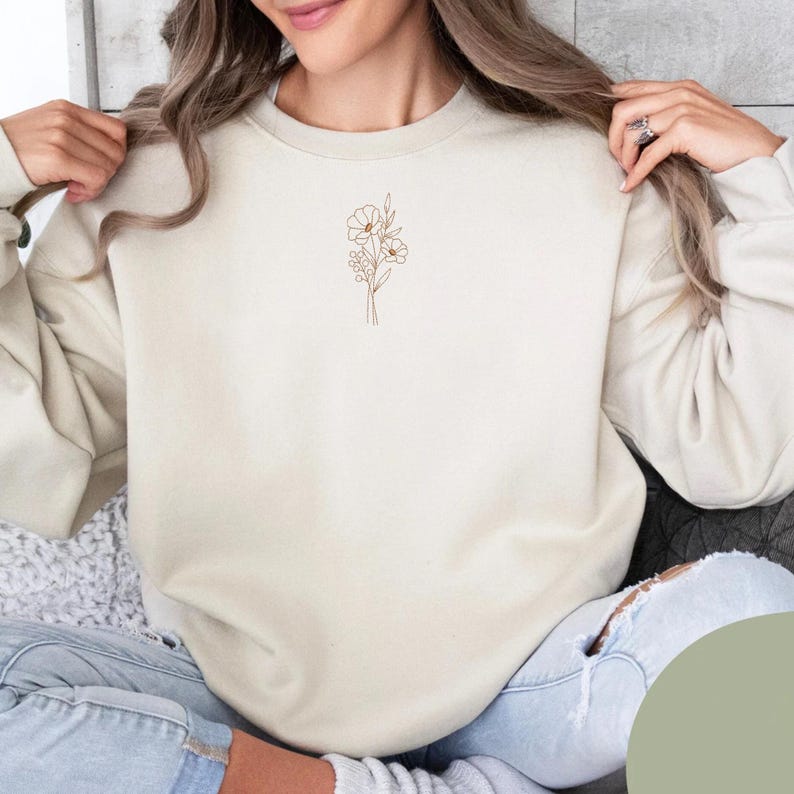 Puede incluir: Sudadera de color crema con un dise&ntilde;o floral minimalista en hilo marr&oacute;n. La sudadera de cuello redondo es de color neutro y tiene un ajuste relajado. El dise&ntilde;o floral est&aacute; bordado en el pecho izquierdo.