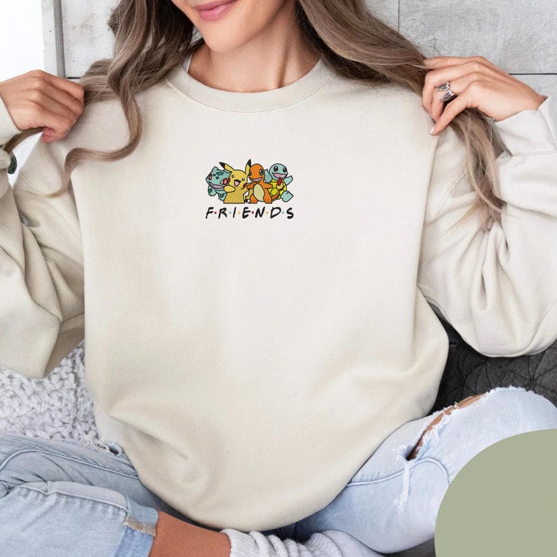 Pode incluir: Camisola creme com a palavra "FRIENDS" e um gr&aacute;fico de Pikachu, Charmander, Squirtle e Bulbasaur. A camisola tem gola redonda e mangas compridas.