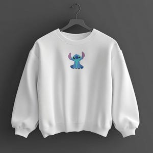 May include: White crew neck sweatshirt with a small embroidered Stitch character. The Stitch design is blue with pink ears. The sweatshirt has long sleeves and a relaxed fit. A casual, comfortable garment.