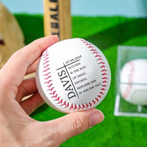 May include: White baseball with red stitching and black text. The text reads "07.08.2025 DAVIS SUCCESS IS THE SUM OF SMALL EFFORTS, REPEATED DAY IN AND DAY OUT".