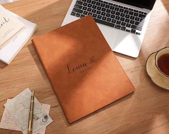 May include: A tan leather portfolio with the name "Lonin" and the date "April 13, 2026" printed on the front. The portfolio is on a wooden desk next to a laptop, a cup of tea, and stationary.