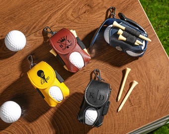 May include: Four leather golf ball holders with personalized initials. Each holder has a golf ball and tees inside. The holders are in different colors: brown, yellow, black, and blue.