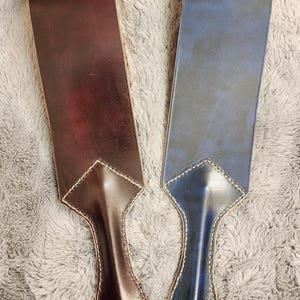 May include: Two leather straps, one dark brown and one dark blue, with a diamond-shaped tip and a rounded handle. The straps are stitched with a light brown thread.