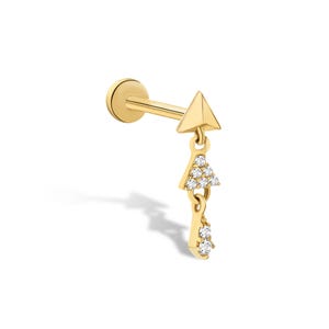 Puede incluir: Pendiente dorado con diseño geométrico. El pendiente presenta una parte superior triangular y un triángulo colgante con piedras transparentes. Un elemento más pequeño en forma de lágrima con dos piedras cuelga debajo.
