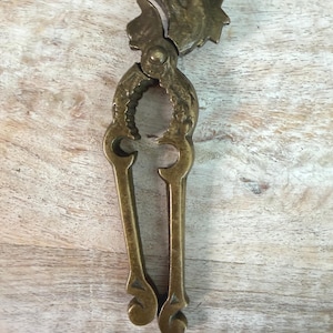 May include: A vintage brass nutcracker with a bird-shaped design. The nutcracker features a detailed bird head at the top and long handles. The brass has a warm, aged patina, suggesting it is an antique or vintage item.