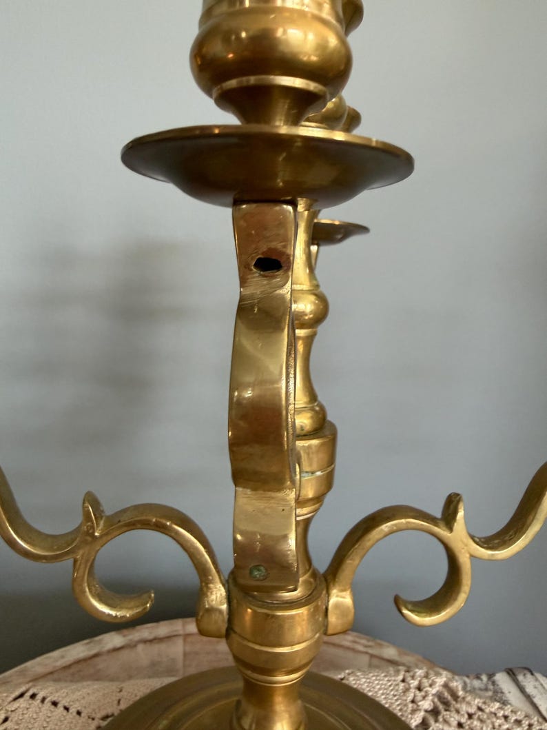 Puede incluir: Un candelabro de lat&oacute;n con tres brazos, con una columna central y brazos curvos decorativos. El candelabro tiene un acabado pulido, que refleja la luz, y est&aacute; dise&ntilde;ado para sostener velas. El dise&ntilde;o es ornamentado y vintage.