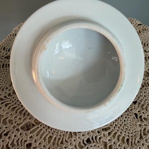 Pode incluir: Uma tampa de cer&acirc;mica branca vista pela parte inferior, apresentando uma borda circular e uma superf&iacute;cie interna lisa e esmaltada. As bordas mostram sinais sutis de desgaste com uma leve descolora&ccedil;&atilde;o acastanhada ao longo da circunfer&ecirc;ncia.