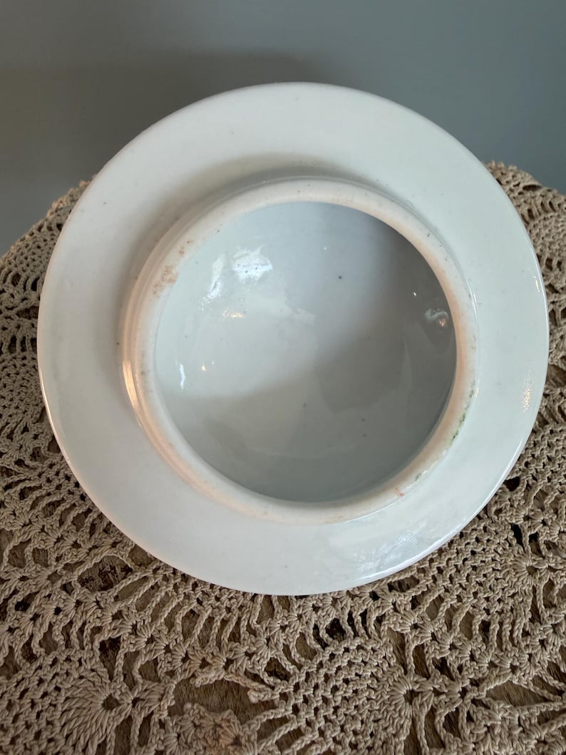 Pode incluir: Uma tampa de cer&acirc;mica branca vista pela parte inferior, apresentando uma borda circular e uma superf&iacute;cie interna lisa e esmaltada. As bordas mostram sinais sutis de desgaste com uma leve descolora&ccedil;&atilde;o acastanhada ao longo da circunfer&ecirc;ncia.