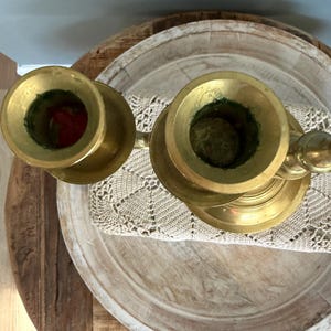 Puede incluir: Dos candelabros antiguos de lat&oacute;n con un acabado deslustrado. Los candelabros est&aacute;n colocados sobre una bandeja de madera con un tapete de ganchillo. Los candelabros tienen un dise&ntilde;o cl&aacute;sico, con una base ancha y una parte superior en forma de copa.