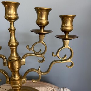 Puede incluir: Un candelabro de lat&oacute;n con tres candeleros. El candelabro tiene una base redonda y brazos curvos. Los candeleros tienen forma de copas. El candelabro es de color dorado c&aacute;lido y tiene un aspecto antiguo.