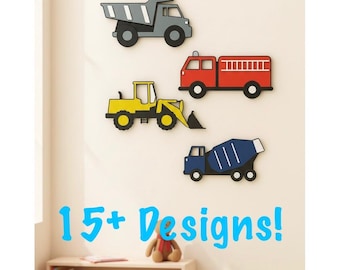 May include: Wall decor featuring four colorful vehicle cutouts: a gray dump truck, a red fire truck, a yellow bulldozer, and a blue cement mixer. The phrase "15+ Designs!" is written in blue script below the vehicles.