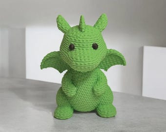 May include: A green knitted dragon figurine with brown eyes, wings, and a horn. The dragon is sitting upright, with its arms and legs positioned in front. The figurine is made of a textured material and is a vibrant shade of green.