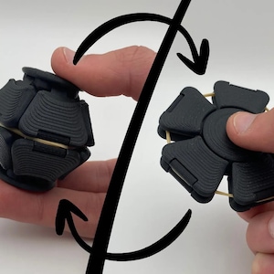 May include: A black fidget toy with a spherical shape composed of multiple textured segments connected by a thin elastic band, shown in two configurations: a closed ball form and an expanded flat, star-like shape with a central circular hub.