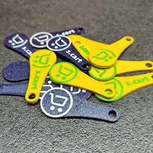 May include: A pile of yellow and navy blue shopping trolley tokens. The tokens are key-shaped with a circular hole and the text "s.cart" and a shopping cart icon printed in green and white.