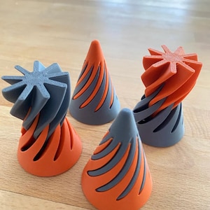 May include: Four abstract, 3D-printed sculptures. Each piece features a cone shape with orange and gray color scheme. The tops of the sculptures have a star-like design. The objects are displayed on a wooden surface.