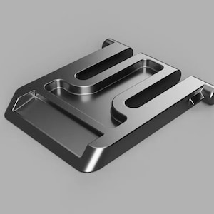 May include: A metallic gray, geometric object with a rectangular base and raised, curved elements. The design features a series of interconnected shapes, creating a modern, industrial aesthetic. The object is set against a neutral gray background.