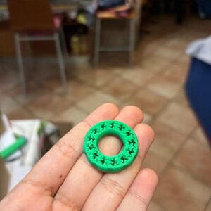 May include: A bright green, circular object with a repeating star pattern around the outer edge. The object is held in a hand, and appears to be made of plastic or a similar material. The background is blurred.