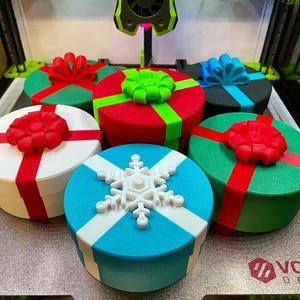May include: A collection of colorful, round gift boxes with decorative bows and ribbons. The boxes are in various colors, including red, green, blue, and white, with contrasting ribbon colors. One box features a white snowflake design.
