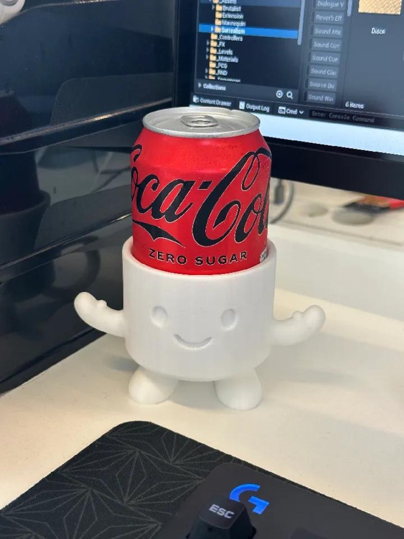 Puede incluir: Una lata roja de Coca-Cola Zero Sugar se encuentra en un soporte blanco con forma de malvavisco sonriente, con brazos y pies. El logotipo de la lata es en negro.