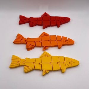 May include: Three plastic fish toys, one red, one orange, and one yellow. The fish are made of interlocking pieces and are designed to be articulated.