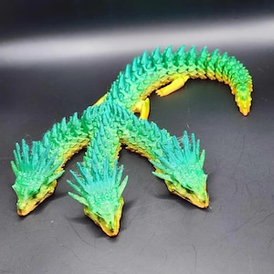 May include: A three-headed dragon figurine in shades of green, yellow, and orange. The dragon's heads are detailed with textured scales and spiky protrusions. The body is segmented, and the overall design is whimsical.