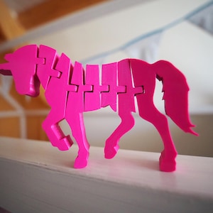 May include: A pink 3D printed unicorn figurine with a segmented design. The unicorn is standing on a white surface.