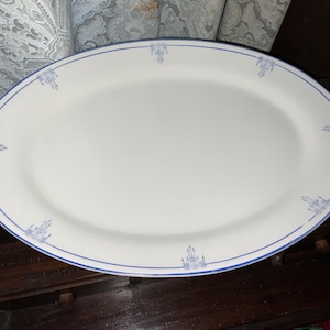 May include: Oval white serving platter with a blue border and decorative blue accents. The platter is made of ceramic and is suitable for serving food. The design is simple and elegant, making it a versatile piece for any table setting.