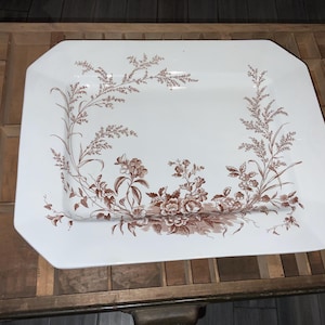 May include: A white, octagonal serving platter with a brown floral design. The design features detailed botanical illustrations of flowers and foliage, creating a vintage aesthetic. The platter is likely made of ceramic or porcelain.