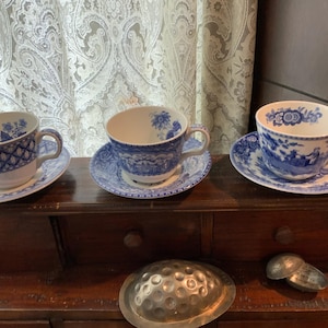 May include: A set of three ceramic mugs with a speckled, matte finish. Each mug features a different color: light blue, cream, and gray. The mugs have a simple, modern design, suitable for coffee or tea.