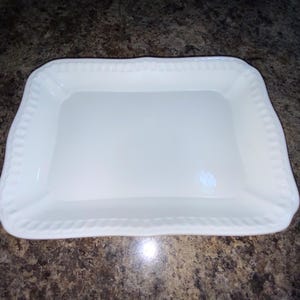 May include: A rectangular white ceramic serving tray with a smooth, flat center and a raised, slightly curved rim featuring a decorative, repeating vertical ribbed pattern along the entire outer edge of the dish.