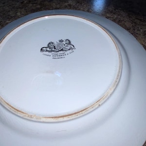 May include: The underside of a white ceramic plate featuring a black printed maker's mark. The mark displays a crest with a lion and unicorn, along with the text Stone China, James Edwards & Son, and Dalehall, centered on the circular base.