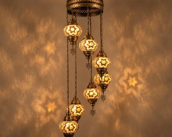 May include: A multi-tiered ceiling pendant light fixture featuring seven hanging glass globes with a warm yellow star pattern. The globes are suspended by metal chains from a circular bronze-toned frame, casting star-shaped shadows on the wall.