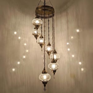 May include: An ornate, antique-style chandelier with multiple glass globes. The fixture has a bronze finish and features intricate metalwork. The clear glass globes are illuminated, casting a warm glow. The design is suitable for home decor.