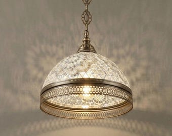 May include: An antique-style pendant light fixture with a mosaic glass shade. The shade is a semi-circular dome shape, with a decorative metal frame. The fixture hangs from a chain with ornate links, and is finished in a bronze color.