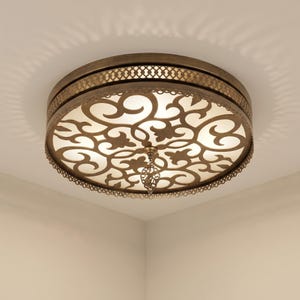 Peut inclure: Luminaire de plafond orné de style antique. Le design circulaire présente des motifs ajourés complexes et un élément décoratif suspendu. Le métal a une finition chaleureuse en laiton et la lumière traverse le motif.