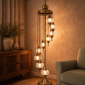 May include: A tall floor lamp with an antique brass finish featuring a central pole and a circular base. Nine spherical glass globes with a textured, clear finish hang at varying heights from the top, each illuminated by a warm light bulb.